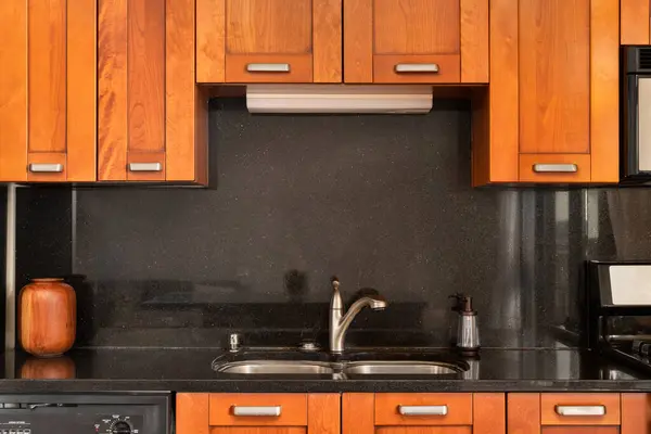A kitchen faucet detail with wood cabinets and a black galaxy granite countertop and backsplash.