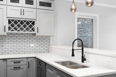 Mutfak musluğu, gri dolaplar, gri cam metro fayansları ve siyah musluk..