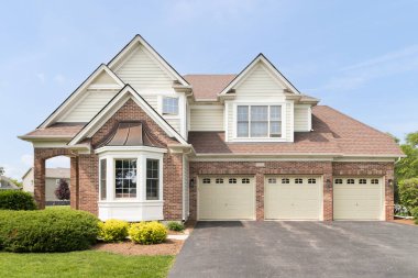 Naperville, IL, ABD - 17 Mayıs 2023: Kırmızı tuğlalı ve sarı kaplamalı büyük bir ev, üç araba garajı ve güzel bir peyzaj..
