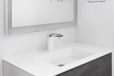 Beyaz ve krom musluğu, beyaz lavabosu ve koyu gri dolabı olan bir banyo musluğu..