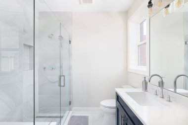 Mavi dolabı olan bir banyo, beyaz mermer tezgah, ve beyaz mermer döşemeleri ve cilalı krom musluğu olan bir duş..