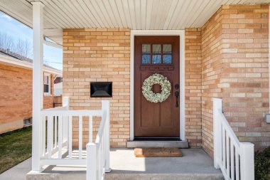 Ön kapısında tahta bir kapı asılı bir çelenk ve beyaz korkuluklu bir veranda olan tuğladan bir evin ön kapısı..