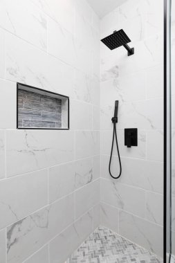 Mermer metro kiremit duvarlı bir duş, gri camlı bir raf, zeminde herringbone fayanslar ve siyah bir duş başlığı var..