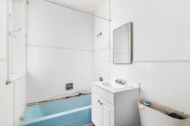 Su hasarlı bir banyo, beyaz karolar, beyaz banyo dolabı ve yenilenmeye hazır mavi bir küvet..