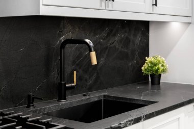 Mutfak lavabosu detaylarıyla modern siyah ve altın musluk, siyah taştan bir tezgah ve geri sıçrama ve beyaz dolaplar..
