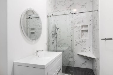 Beyaz dolabı, konsol lavabosu, krom musluğu, duş başlığı, beyaz mermer ve siyah kareli duşu olan bir banyo..