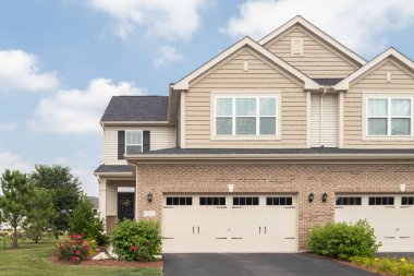 Plainfield, IL, ABD - 22 Ağustos 2023: Bir banliyö, iki katlı iki katlı garaj, kahverengi vinil ve kaya kaplaması ve güzel peyzaj.