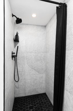 A shower with a black showerhead, black marble hexagon tile flooring, and black and white brushstroke pips tiles. clipart