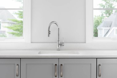 Parlatılmış krom musluk, beyaz mermer tezgah, gri dolaplar ve donanım içeren bir mutfak lavabosu ayrıntısı..