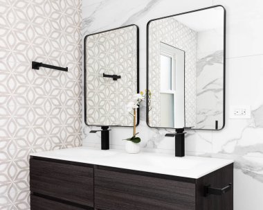 Modern ahşap bir dolabı, mermer döşeli duvarları, beyaz lavabosu ve siyah musluğu ve siyah çerçeveli aynaları olan bir banyo ayrıntısı..