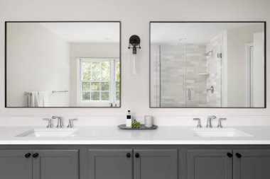 Gri makyaj dolabı olan bir banyo, iki lavabosu olan beyaz mermer tezgah ve fayanslı duşun ve pencerenin geniş aynalarından bir manzara..