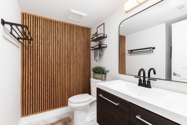 Koyu ahşap bir dolabı olan bir banyo, tuvaletin üstünde süslemeleri olan yüzen raflar, ve ahşap aksanlı bir duvar..