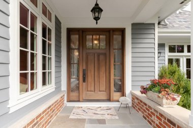 A front door and covered porch detail on a home with grey siding, white trim, red brick, a wooden front door. clipart