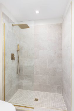Kare kahverengi fayanslar, cam duvarlar ve altın bir duş başlığı, duş hortumu ve drenaj..