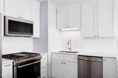 Beyaz dolapları, mermer tezgahı, metro fayansları ve paslanmaz çelik aletleri olan bir mutfak detayı..