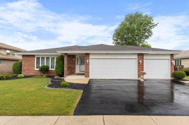 Romeoville, IL, ABD - 10 Temmuz 2024: Tuğla kaplamalı bir banliyö evi, üç araba garajı, düzgün bir peyzaj ve ıslak bir asfalt garaj yolu.