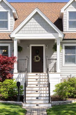 Ön kapıda merdivenler, karanlık ahşap bir ön kapı, veranda ve işlenmiş demir parmaklıklar var..