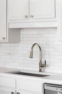 Mutfak lavabosunun detaylarını mermer metro döşemesi granit tezgah, beyaz dolaplar ve fırçalanmış altın bir muslukla çekiyoruz..