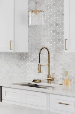 Altın musluğu olan bir mutfak, beyaz mermer mozaik döşeme, beyaz dolaplar ve beyaz bir tezgah..
