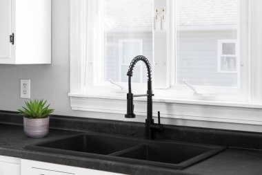 Siyah taştan bir lavabosu ve siyah musluğu olan modern beyaz bir mutfak ve siyah tezgahın üzerinde küçük sulu bir musluk var..