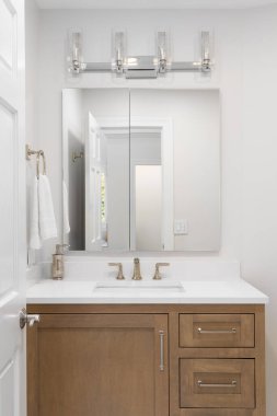 Üzerinde meşe kabini olan bir banyo ayrıntısı, beyaz mermer bir dolapta bronz musluk ve dikdörtgen aynanın üzerine monte edilmiş krom lamba armatürü..