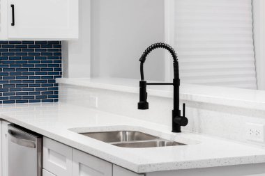 Siyah musluğu, beyaz kuvars tezgahı ve mavi cam metro döşemesi olan bir mutfak detayı..