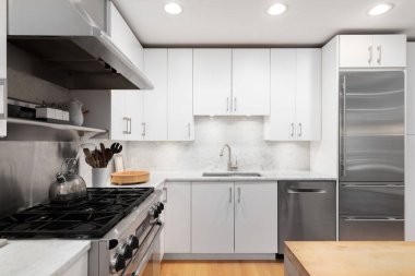 Beyaz dolapları, paslanmaz çelik aletleri, ahşap döşemeleri, kasap blok adası ve beyaz mermer tezgahı olan bir mutfak müfrezesi. Marka ya da etiket yok.