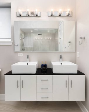 Yüzen beyaz bir dolabı olan bir banyo ayrıntısı, siyah mermer tezgahta duran bir kap ve aynadaki duşun görüntüsü..