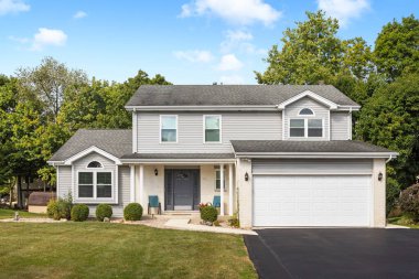 Naperville, IL, ABD - 6 Eylül 2024: İki katlı bronz ve tuğlalı bir banliyö evi, iki araba garajı, siyah garaj yolu, güzel bir peyzaj ve gri bir ön kapı.