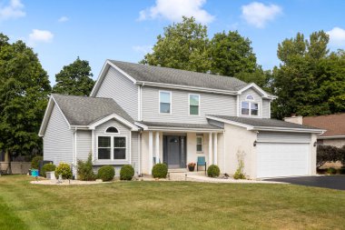 Naperville, IL, ABD - 6 Eylül 2024: İki katlı bronz ve tuğlalı bir banliyö evi, iki araba garajı, siyah garaj yolu, güzel bir peyzaj ve gri bir ön kapı.
