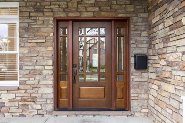 Ön kapıda kaya kaplamalı, pencere panelli ahşap bir ön kapı ve beyaz bir pencere var..