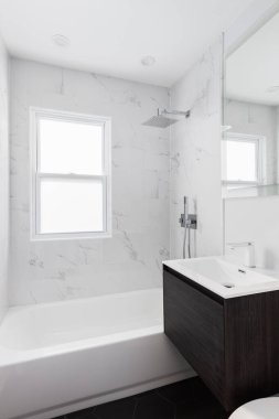 Parlak bir banyo mermer kaplama bir duş, koyu ahşap yüzen makyaj dolabı, siyah altıgen döşeme, ve krom musluk.