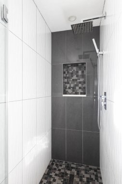 Geniş formatlı, koyu gri fayanslı modern bir duş mozaik kare döşeme ve raf ve krom duş başlığı..