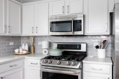 Beyaz dolapları ve tezgahları olan bir mutfak detayı, gri metro döşemesi, paslanmaz çelik aletler, ve tezgahın üzerindeki dekorasyonlar..