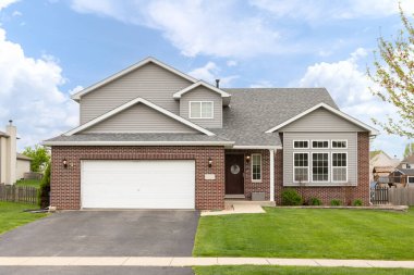 Plainfield, IL, ABD - 18 Nisan 2024: Gri vinil ve kırmızı tuğla kaplamalı ve iki araba garajlı iki katlı tek katlı bir aile evi.