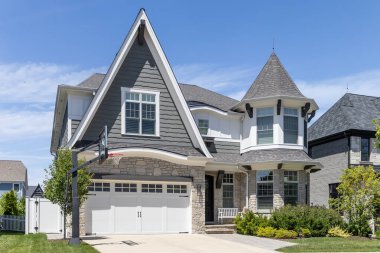 Naperville, IL, ABD - 11 Haziran 2024: Birinci katta dik çatı, taret ve kaya kaplamalı gri ve beyaz bir Viktorya tarzı ev.