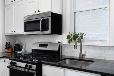 Siyah tezgahları ve beyaz dolapları olan bir mutfak müfrezesi gri cam metro döşemeleri ve paslanmaz çelik ve siyah aletler..