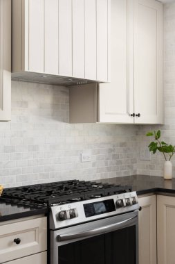 Krem rengi dolapları ve kaputu olan bir mutfak müfrezesi paslanmaz çelik soba, mermer metro döşemesi ve siyah granit tezgahı..