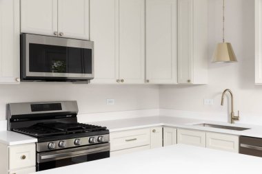 Beyaz dolapları, beyaz mermer tezgahı, altın rengi musluğu ve paslanmaz çelik aletleri olan bir mutfak..