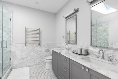 Büyük gri makyaj dolabı olan bir banyo, mermer döşemeli duvarlar ve döşemeler, beyaz mermer tezgahta krom musluklar, ve içeri giren duş..