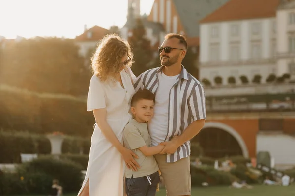 Father, mother and son are hugging in an old European town. Happy family in the evening. Dad is laughing with his family in the background of the palace at sunset.