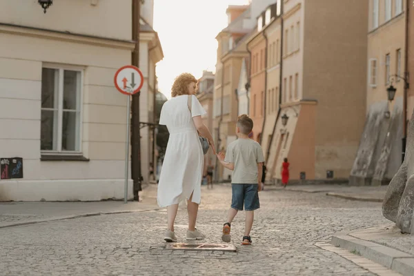 A family is strolling on the paving stones in an old European town. A happy mother and son are holding hands and having fun in the evening.