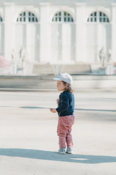 一个戴着帽子的女蹒跚学步的幼儿 全身都是天鹅绒 左边在欧洲宫殿的院子里 一个女婴走到喷泉前 图库图片