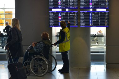 Varşova, Polonya - 17 Ekim 2023: Bir terminal çalışanı tekerlekli sandalyedeki bir kadına uçuş programına bakmasında yardım ediyor. Varşova Chopin Havaalanı. Seyahat kavramı