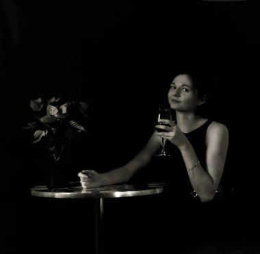 Portrait of a young woman sitted at a table, waiting for a date, and having a glass of red wine