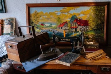 Wernigerode, Saxony-Anhalt, Germany, 29 October 2022: interiors of Kleinstes Haus, Folklore Museum, sofa with cushions and table with book, tea set cup and saucers, sewing machine, landscape paintings