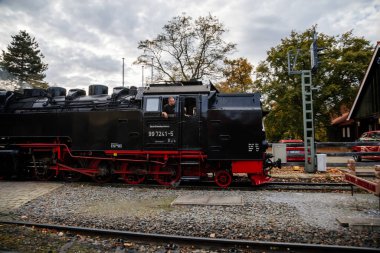 Wernigerode, Germany, 29 October 2022: Steam engine train in Harz Mountains Region, Old retro vintage steam locomotive near railway station at sunny day, white smoke from train chimney, Brocken Line