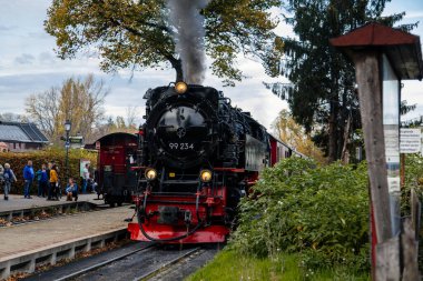 Wernigerode, Germany, 29 October 2022: Steam engine train in Harz Mountains Region, Old retro vintage steam locomotive near railway station at sunny day, white smoke from train chimney, Brocken Line