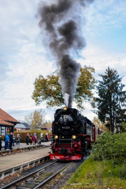 Wernigerode, Germany, 29 October 2022: Steam engine train in Harz Mountains Region, Old retro vintage steam locomotive near railway station at sunny day, white smoke from train chimney, Brocken Line
