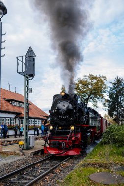 Wernigerode, Germany, 29 October 2022: Steam engine train in Harz Mountains Region, Old retro vintage steam locomotive near railway station at sunny day, white smoke from train chimney, Brocken Line